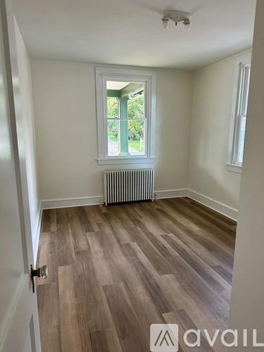A room with wooden flooring and a window with a view of greenery outside.