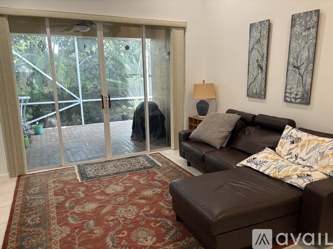 A woman in a black dress stands in a living room with a brown couch and a rug.