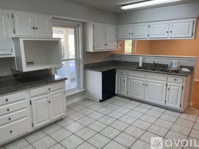 A kitchen with white cabinets and a black trash can.