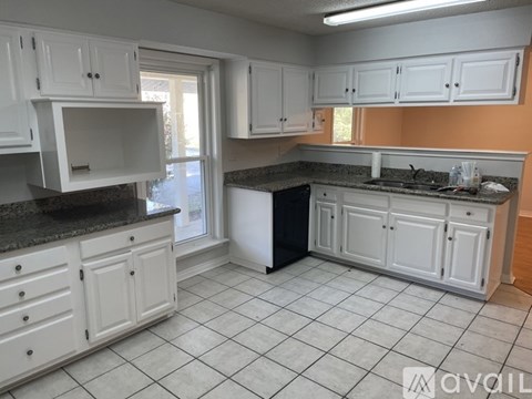 A kitchen with white cabinets and a black trash can.