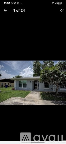A white house with a grey roof and a tree in front.