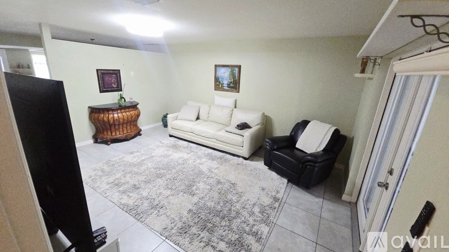 A living room with a white couch, a wooden table, and a black chair.
