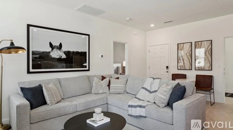 A living room with a grey couch, a coffee table, and a painting of a horse on the wall.