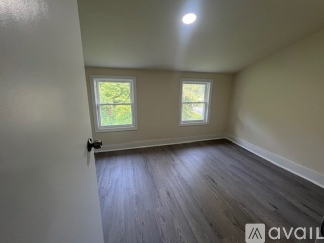 A room with wooden flooring and two windows.