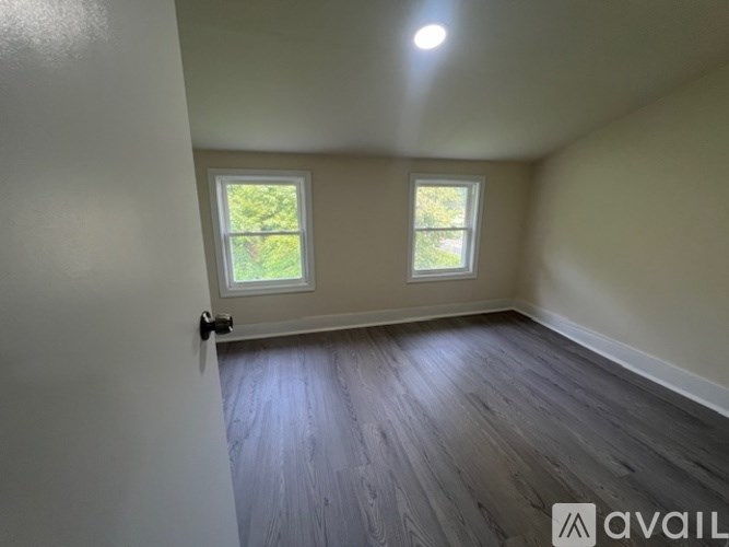 A room with wooden flooring and two windows.
