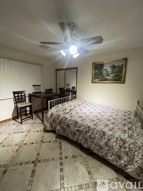 A bedroom with a bed, desk, chair, and a ceiling fan.