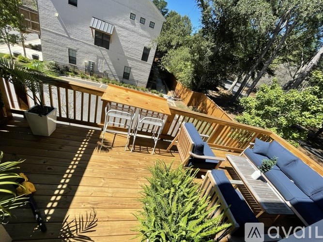 A wooden deck with a table and chairs is surrounded by green plants.