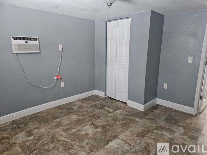 A room with a carpet floor, a white door, and a window with a fan.