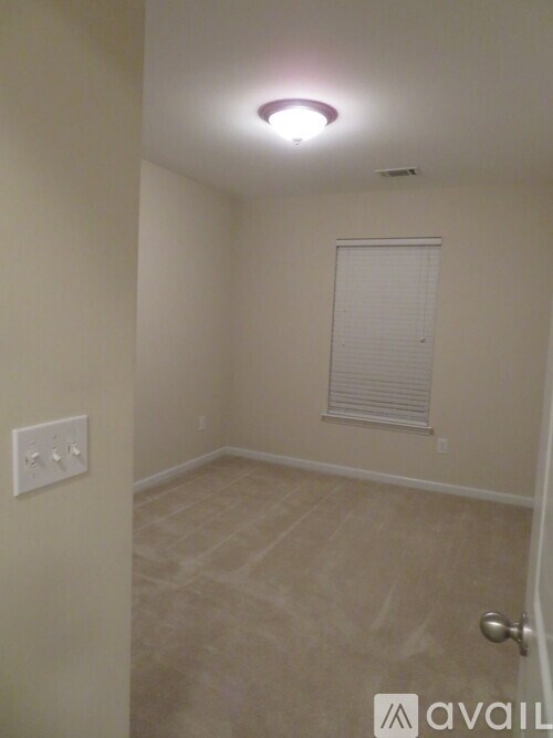 A room with a door, a window with blinds, and a light switch on the wall.