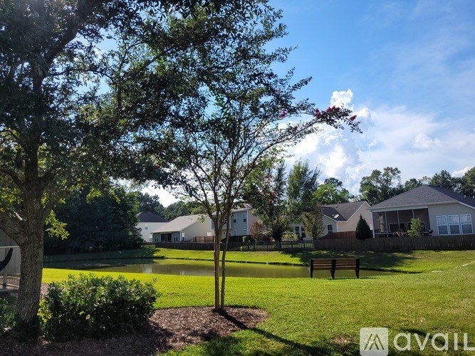 A tree with red flowers stands in a grassy field with houses in the background.