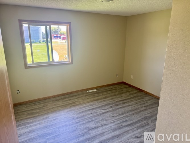 A room with a window showing a view of a field and a building.