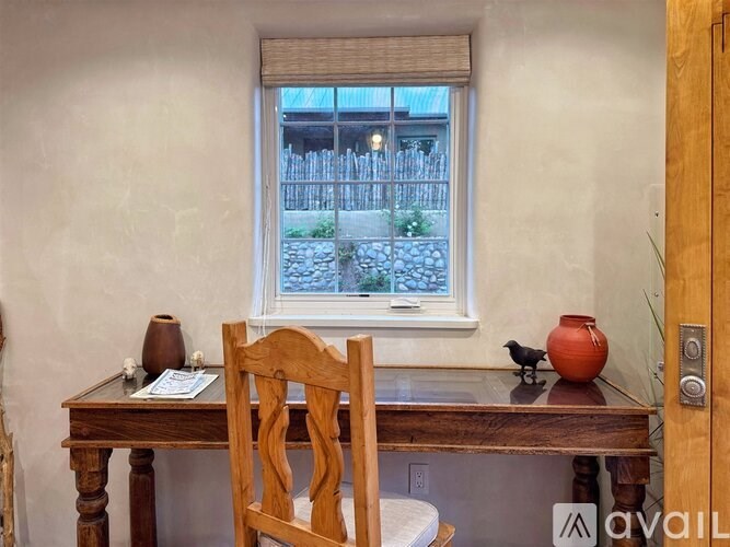 A wooden chair sits in front of a table with a vase and a small bird on it.