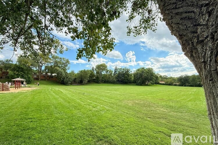 A grassy field with trees and a gazebo in the distance.