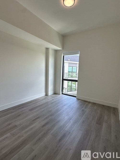 A room with wooden flooring and a window leading to a balcony.