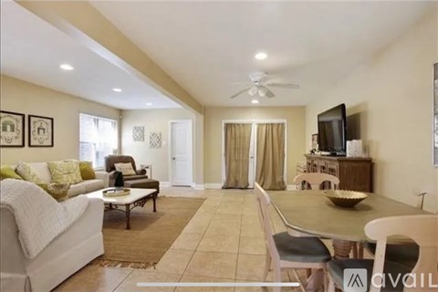 A living room with a white couch, a coffee table, a television, and a dining table with chairs.