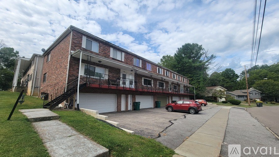 A red car is parked in the driveway of a brick apartment building.