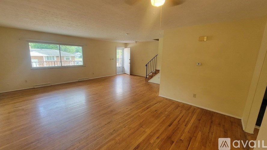 A spacious room with wooden floors and a staircase leading to another room.