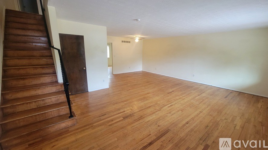 A room with wooden flooring and a staircase with a black railing.