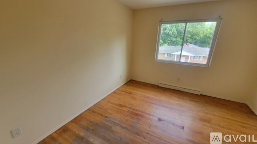 A room with wooden floors and a window showing a view of houses outside.