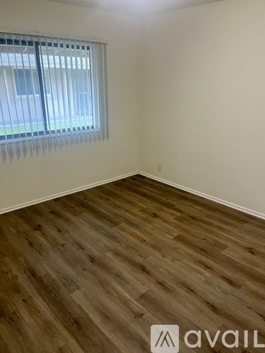 A room with wooden flooring and a window with blinds.