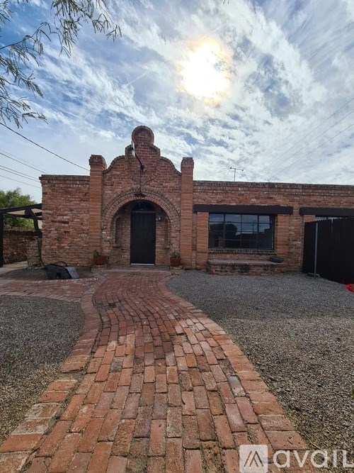 A brick building with a black door and windows is surrounded by a gravel driveway.