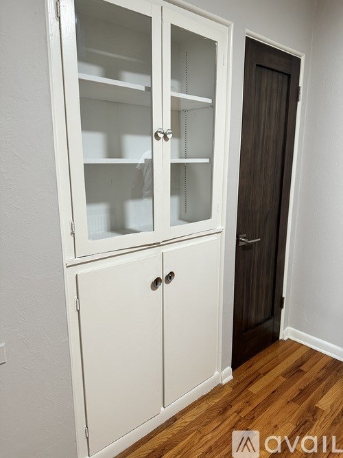 A white cabinet with glass doors and a brown door.