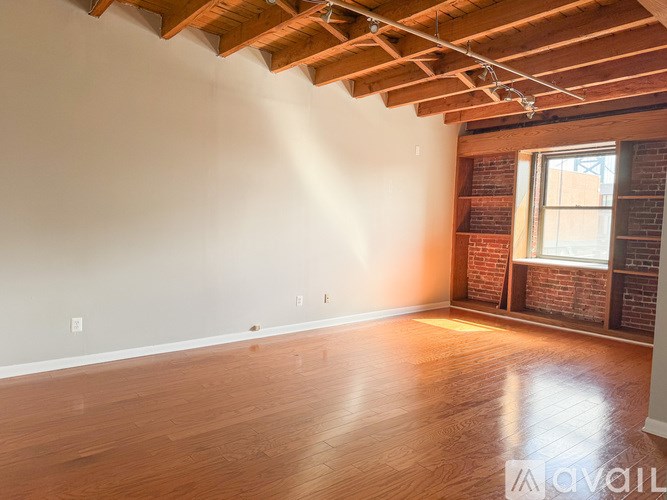 A room with wooden floors and a window with a brick wall behind it.