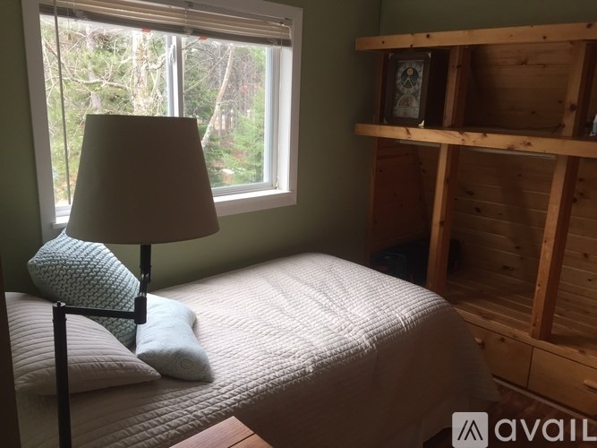A bedroom with a bed, a lamp, and a wooden shelf.