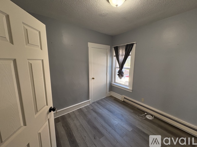 A room with a door, a window with curtains, and a wooden floor.