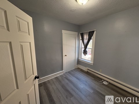 A room with a door, a window with curtains, and a wooden floor.