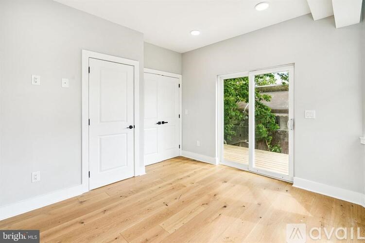 A room with white walls and wooden flooring, featuring two doors and a sliding glass door.
