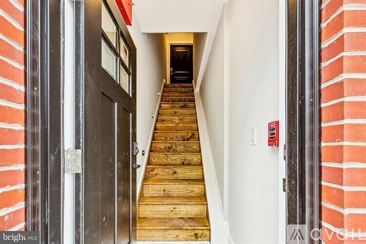 A staircase with a wooden handrail and a red fire alarm on the wall.