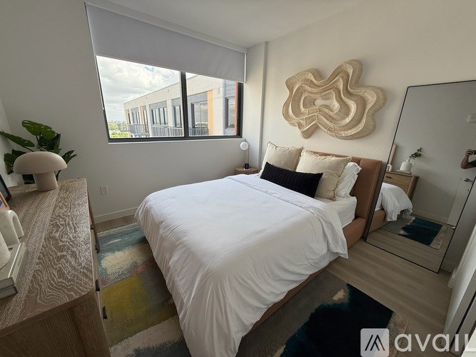 A bedroom with a large bed, a mirror, and a window with a view of a building outside.