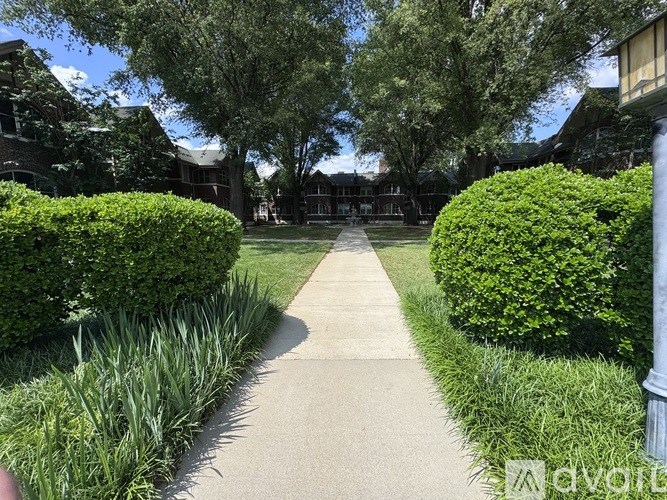 A walkway between two green bushes with a building in the background.