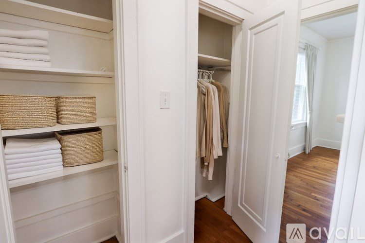 A white closet with clothes hanging and baskets on shelves.