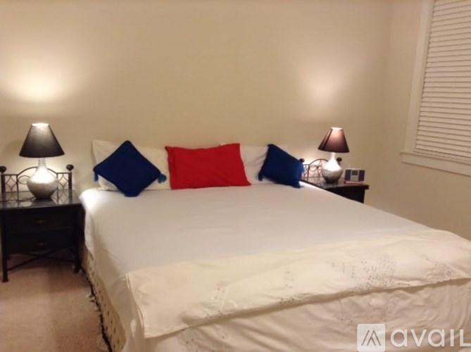 A bed with a white comforter and three pillows in blue, red and white.