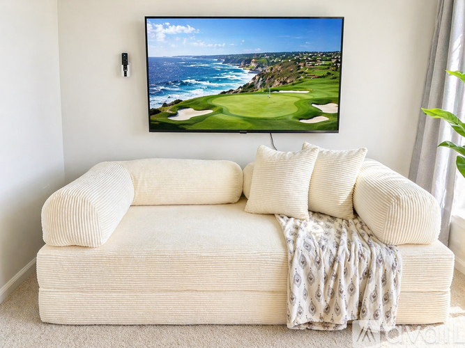 A white couch with a blanket and pillows in front of a television displaying a golf course.