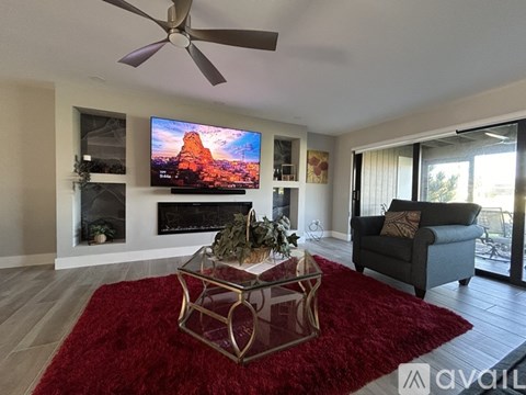 A living room with a red rug and a flat screen TV mounted above a fireplace.