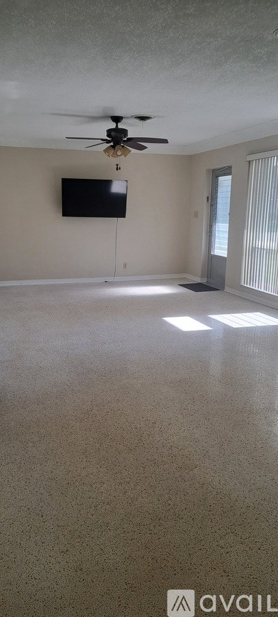 A room with a ceiling fan and a flat screen TV mounted on the wall.