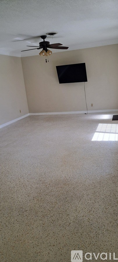 A room with a ceiling fan and a flat screen TV mounted on the wall.