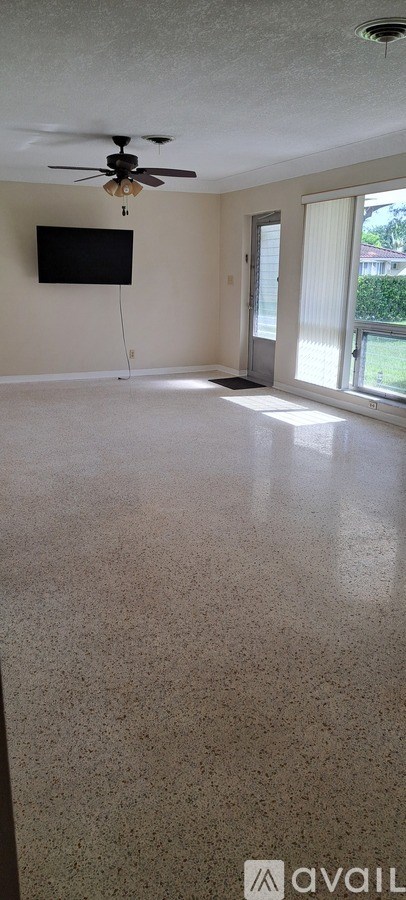 A room with a ceiling fan and a flat screen TV mounted on the wall.