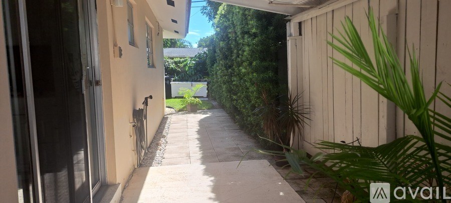A narrow alley with a white wall on the left and green plants on the right.