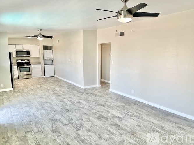 A spacious living room with a fan and a kitchen area in the background.