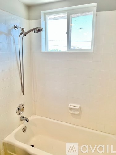 A white bathtub with a shower head and a window above it.