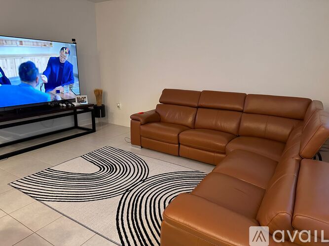 A living room with a brown leather couch and a television playing a movie.