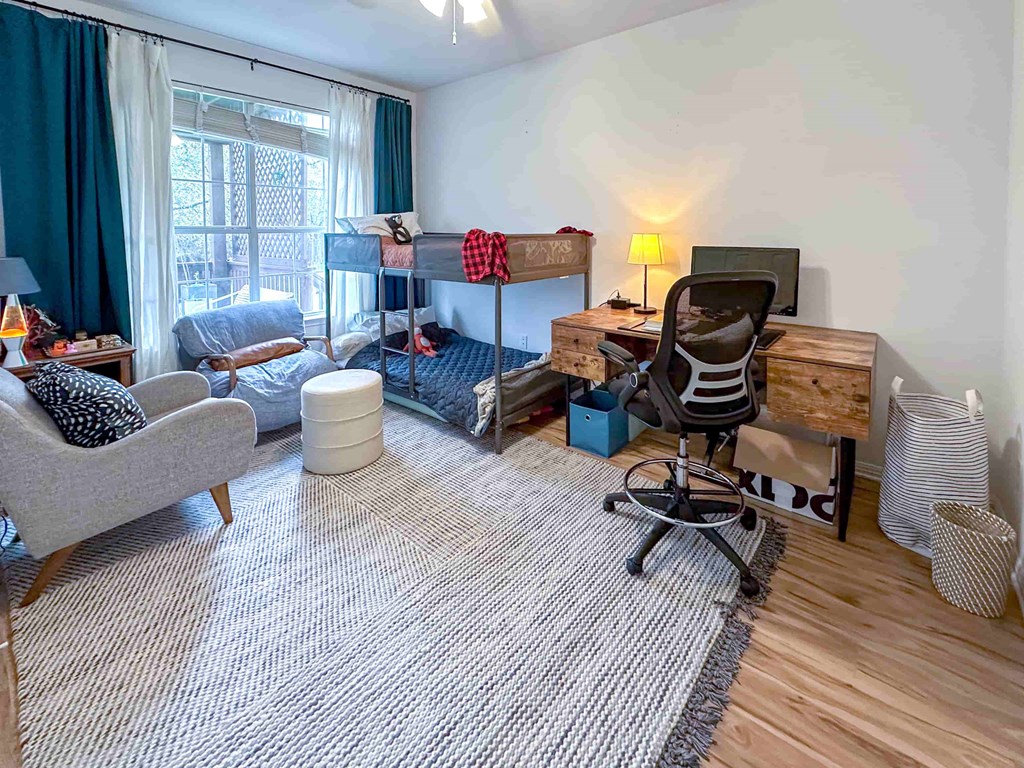 A room with a grey couch, a wooden desk, and a striped rug.