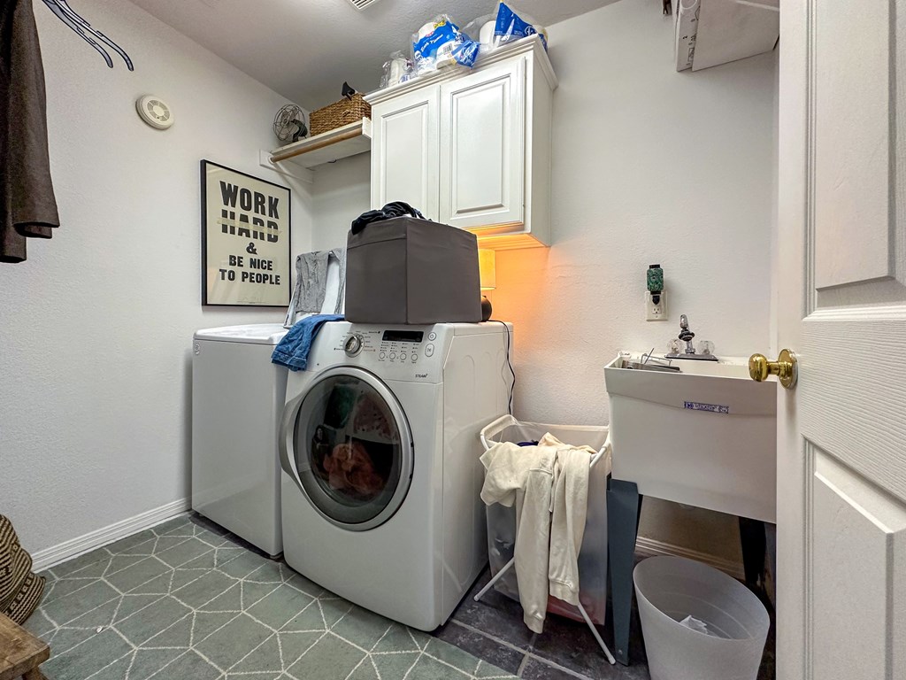 A laundry room with a washer and dryer, a sink, and a sign on the wall.