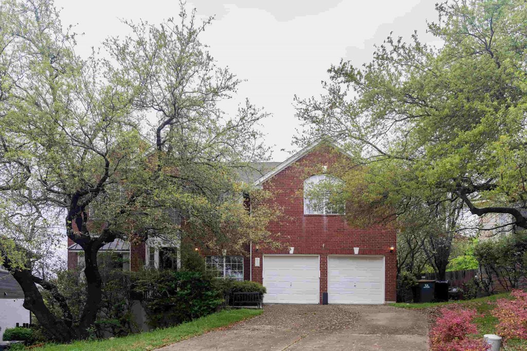A red brick house with a white garage door is surrounded by trees.