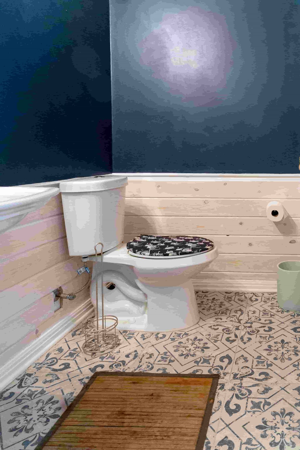 A white toilet sits in a bathroom with a wooden floor and a tiled floor.