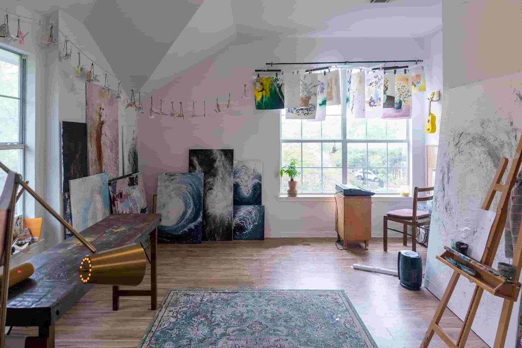 A room with a painting on the easel and a chair.